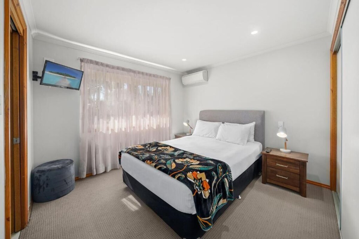 A bedroom with a bed, bedside table, lamp, and a television on the wall.