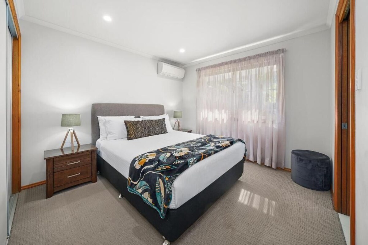 A bedroom with a bed, bedside tables, a lamp, a window with curtains, and a waste bin.