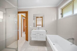 A modern bathroom with a glass shower enclosure, a white vanity with a mirror, and a standalone bathtub. - Nilora Resorts & Hotels (Port Macquarie)