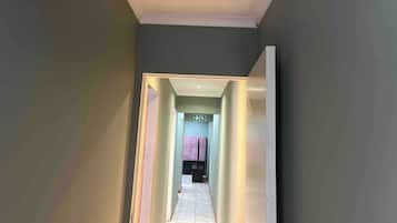 A hallway leading to a room with a visible exit sign and a door at the end.