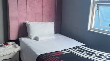 Un dormitori amb un llit, una nitòria, una finestra i un capçal de llit.