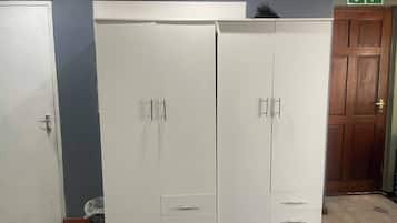 A room with a large white wardrobe, a wooden door, and a tiled floor.