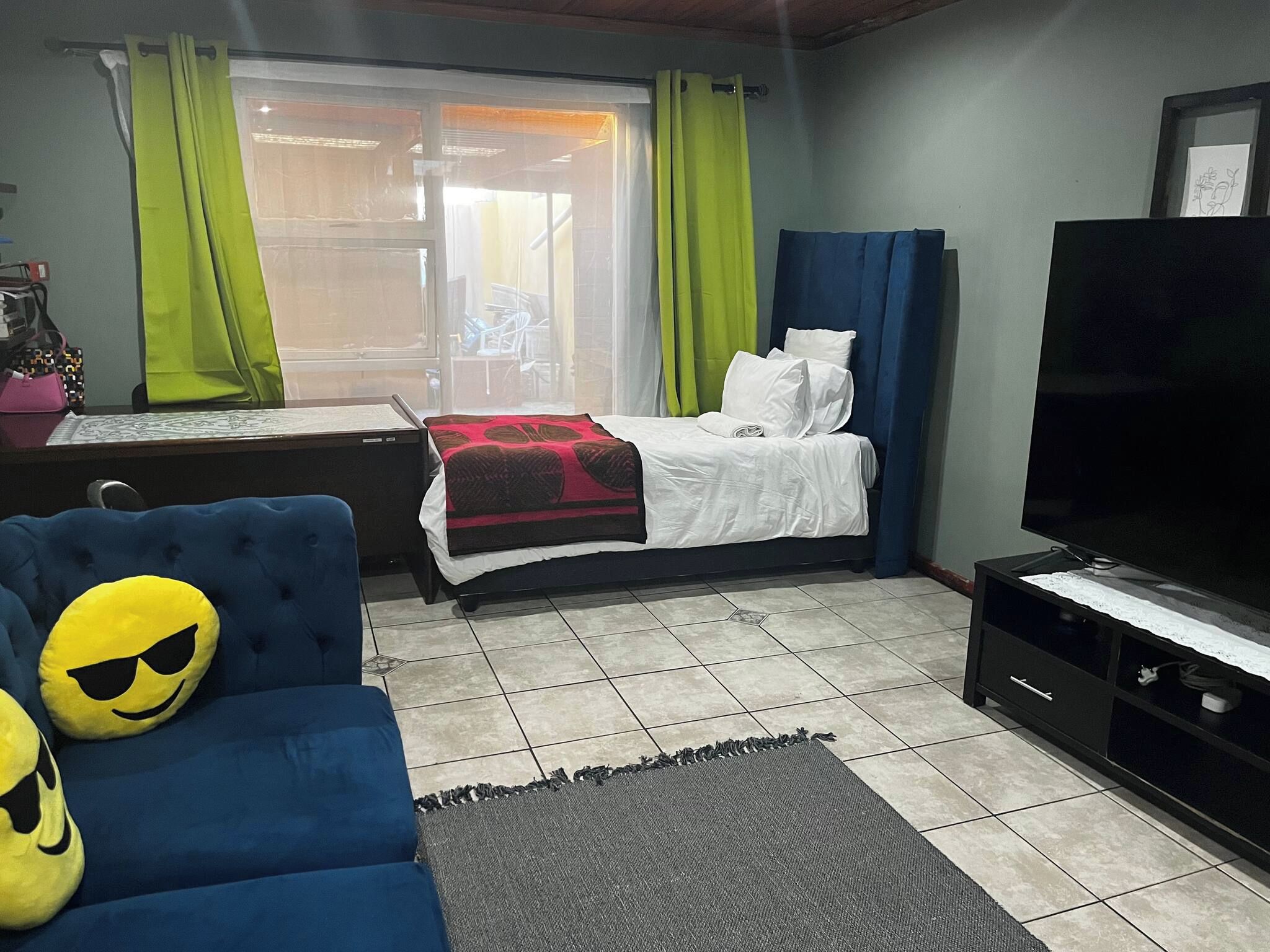 A bedroom with a bed, a sofa with a cushion, a television, and a window with curtains.