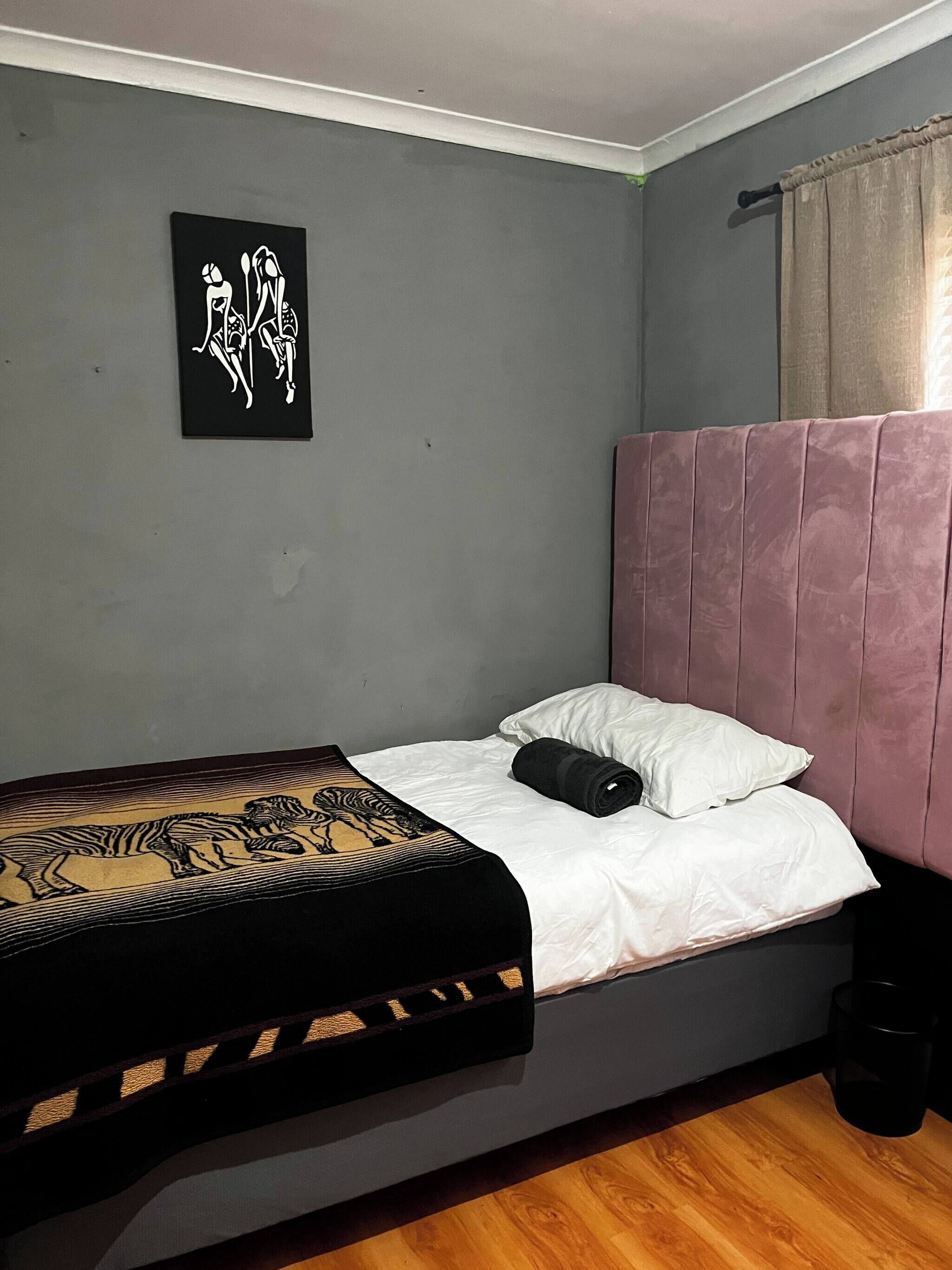 Een enkel bed met hoofdeinde, een zwart-geel bedsprei, witte kussens en een zwart voorwerp op het bed.