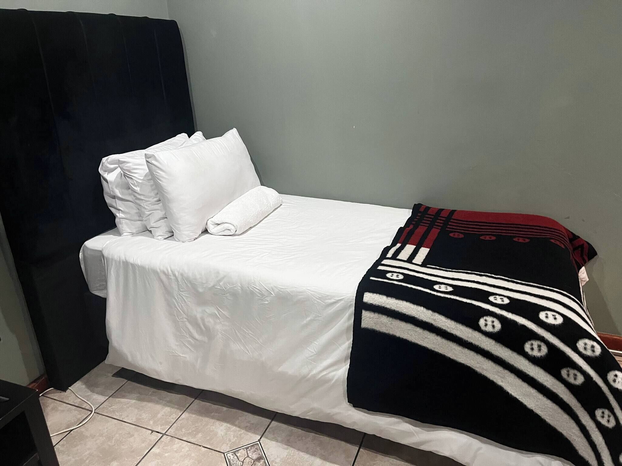 Una cama individual con ropa blanca y una colcha negra y roja.