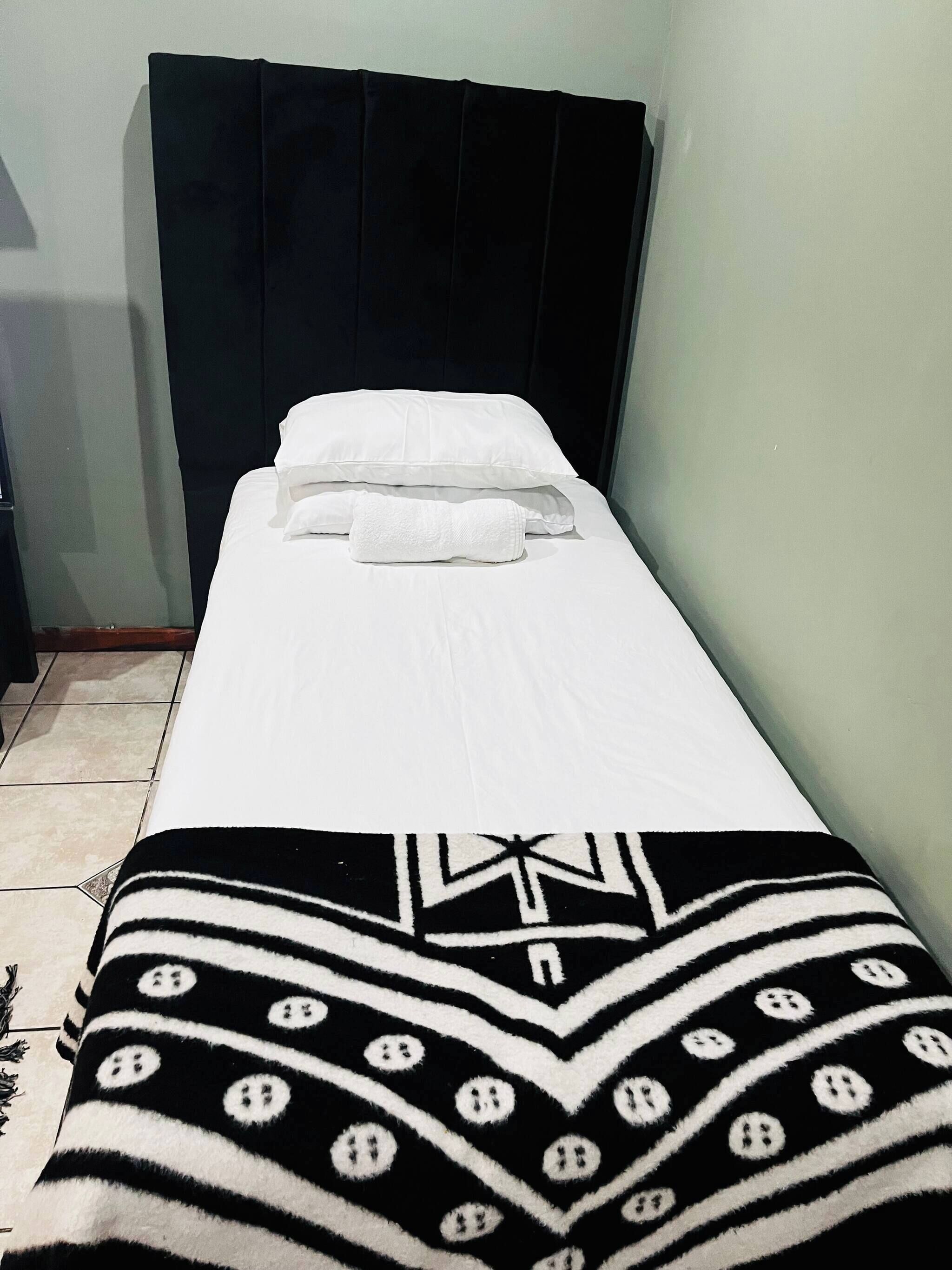 A single bed with white bedding and a black and white patterned blanket.