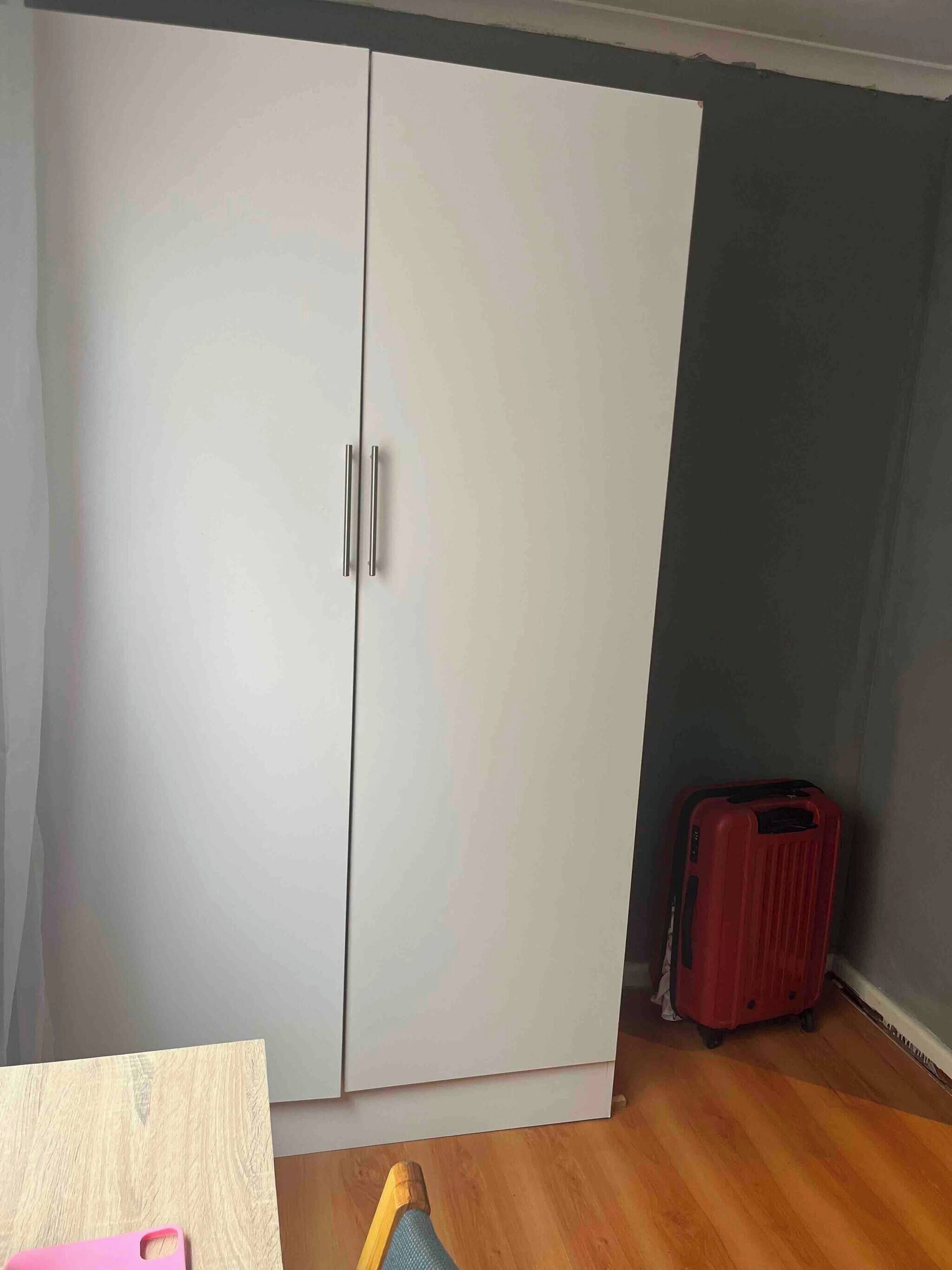 Een kamer met een grote kast, een rode koffer en een houten vloer.