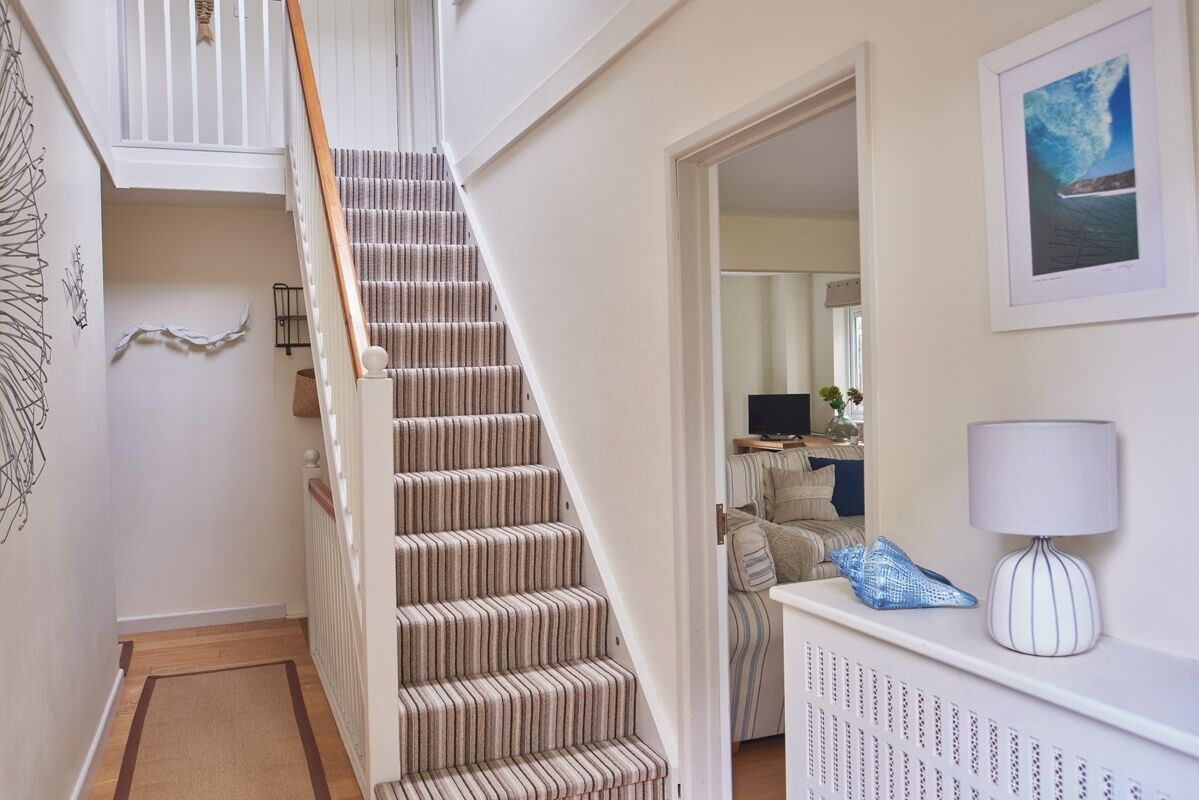 A staircase with a striped carpet, a white wall with a framed picture, and a radiator.