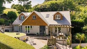Ein zweistöckiges Haus mit überdachter Terrasse, einem eingezäunten Garten und einem kleinen Blumenbeet.