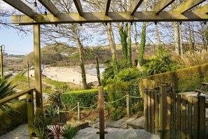 A wooden pergola with hanging light bulbs, a pathway leading to a beach, and a fenced area with greenery. - Avalon Beach House - sleeps 6 guests  in 3 bedrooms (Falmouth)