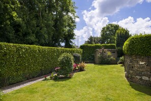 Un giardino curato con un muro in pietra, una struttura in legno e diverse piante.