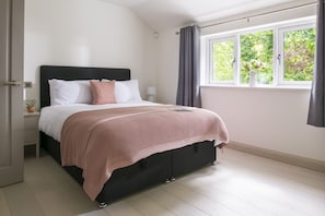 Ein Schlafzimmer mit einem Bett, Nachttischen, einem Fenster mit Vorhängen und Blick auf Grünfläche.