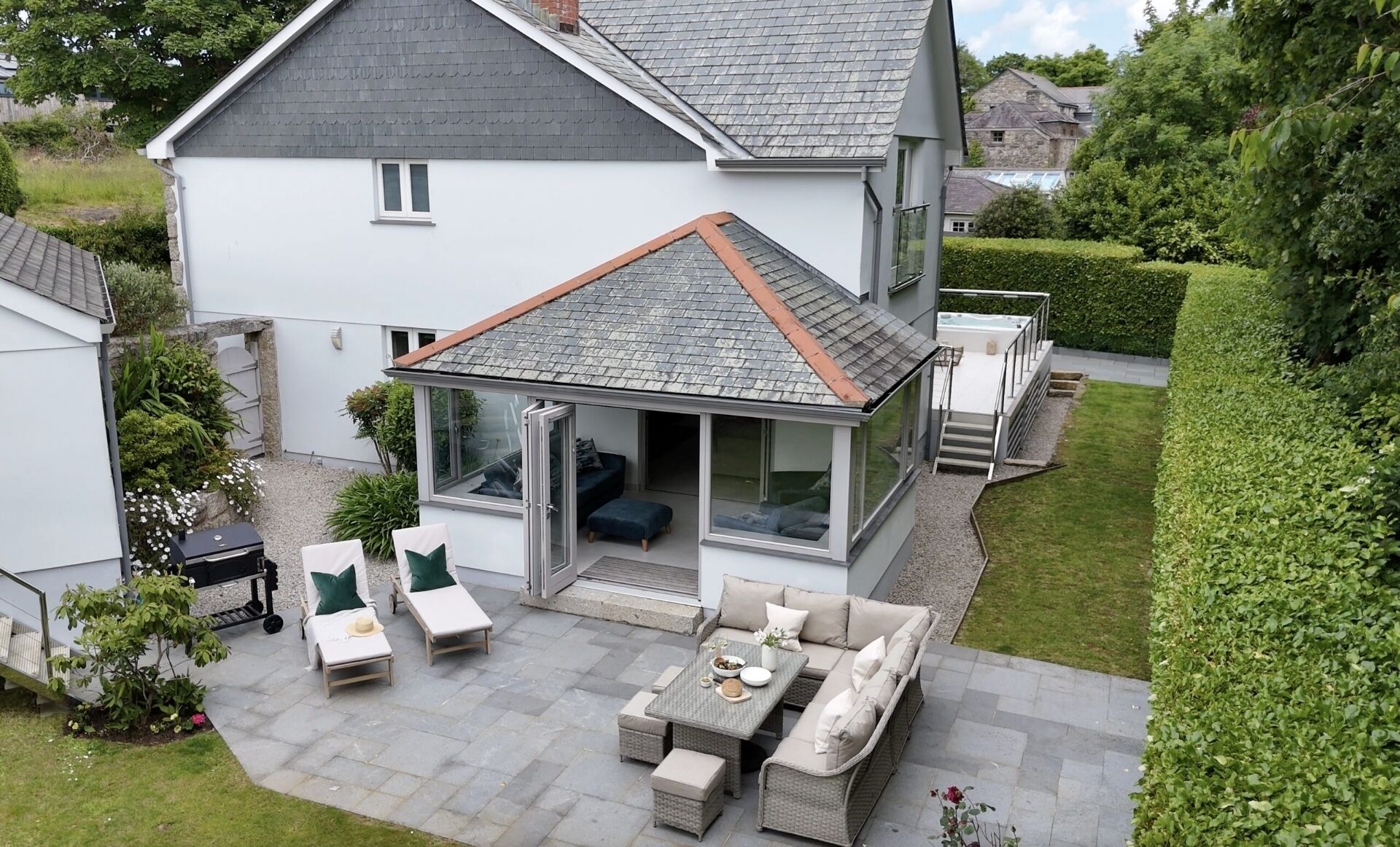 Une maison moderne dotée d’un patio aménagé avec des meubles d’extérieur, un jacuzzi et une véranda fermée par des baies vitrées.