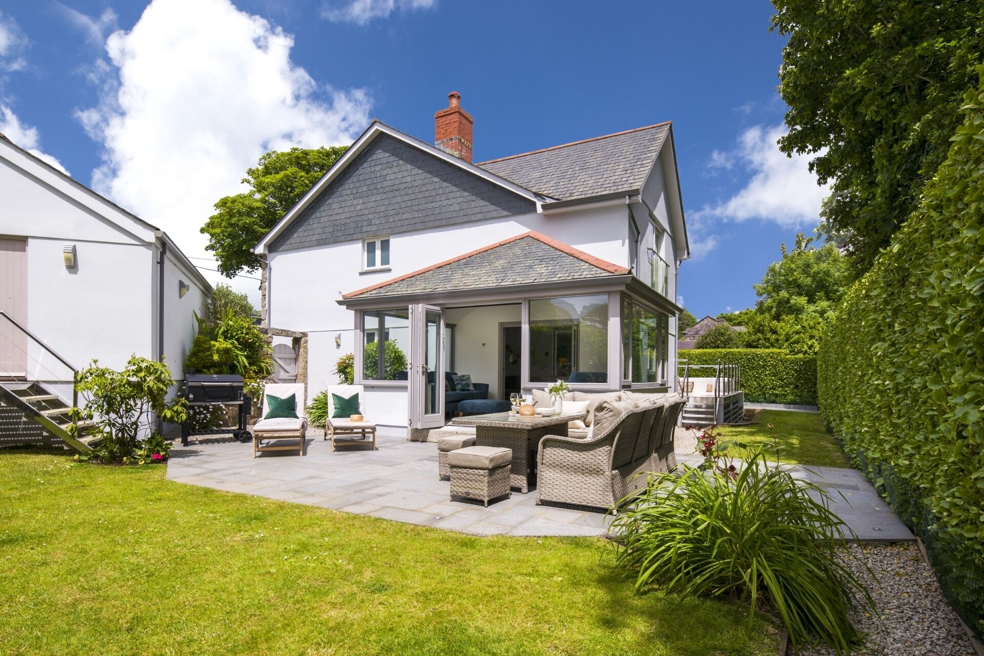 A two-story house with a covered patio, outdoor seating, and a well-maintained garden.