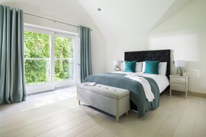 A bedroom with a large window, a bed with a headboard, a bedside table, and a bench. - Bryher Garden - sleeps 8 guests  in 4 bedrooms (Penzance)