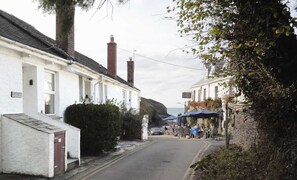 A narrow street lined with white buildings, a café with outdoor seating, and a view of the sea. - Courtyard Cottage - sleeps 4 guests  in 2 bedrooms (Port Gaverne)