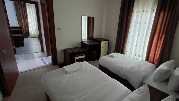 A hotel room with two beds, a desk, a mirror, and a view of the corridor.