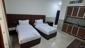 A hotel room with two beds, a kitchenette, and a wardrobe.