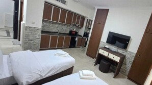 A hotel room with two beds, a desk, a television, and a kitchenette.