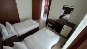 A bedroom with two beds, a small desk, a mirror, and a wardrobe.