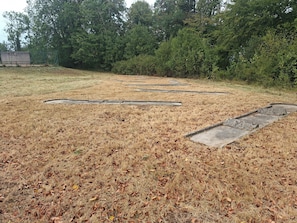 Un champ herbeux avec une structure en béton, entouré d’arbres denses.