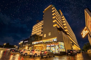 A hotel with multiple floors, a restaurant on the ground floor, and a parking lot with cars. - Hotel Lotus Paradise By Golden Key  (Sonipat)