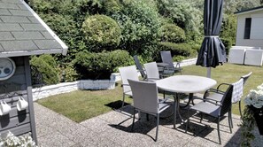 Eine Terrasse mit rundem Tisch und vier Stühlen, umgeben von einer Steinmauer und Pflanzen.