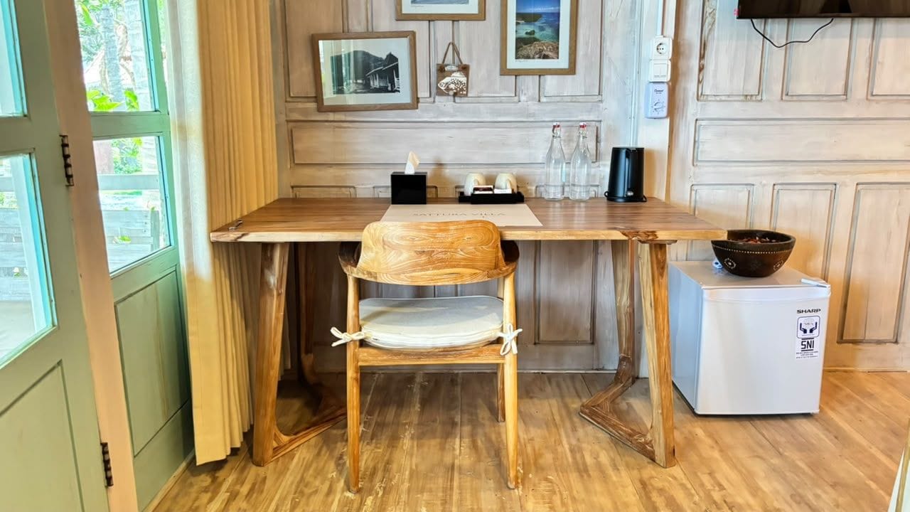 Uma mesa de jantar de madeira, uma cadeira, uma pequena geladeira e uma TV fixada na parede.
