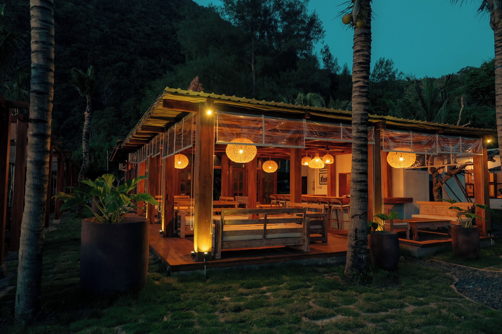 A wooden structure with a covered patio, large potted plants, and hanging lights.