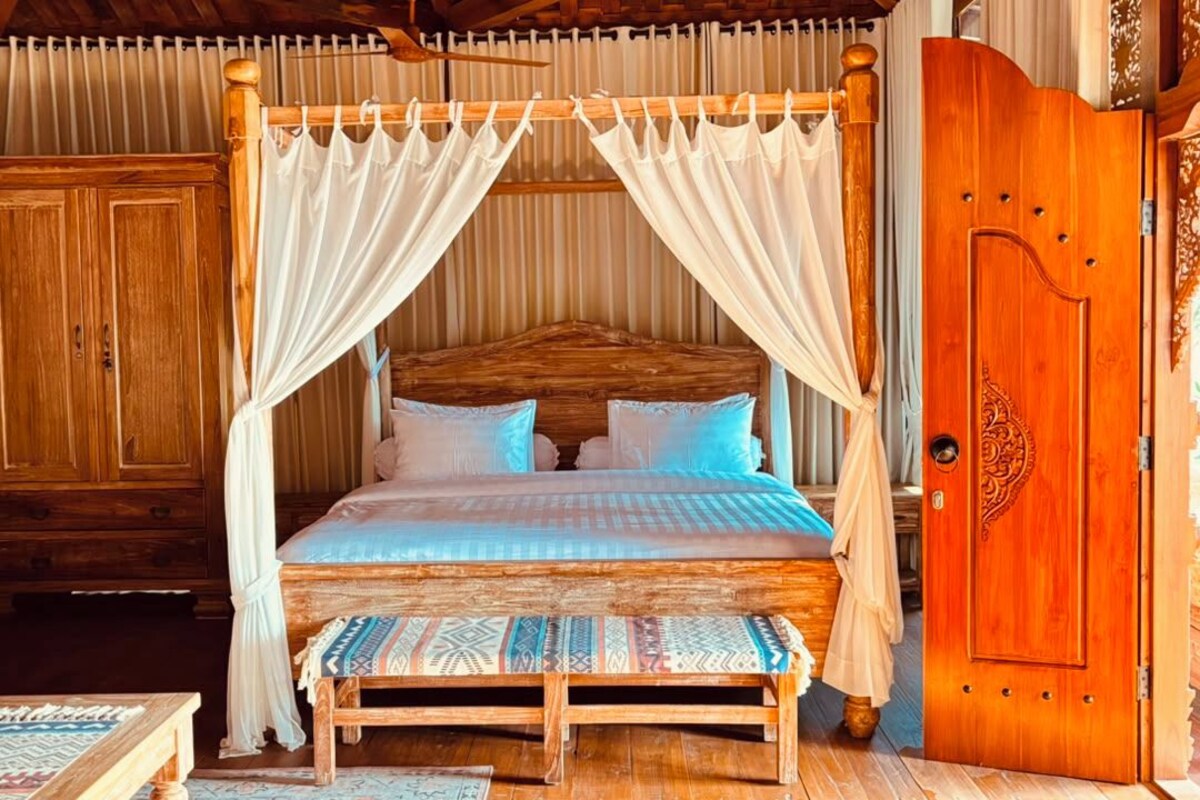 Una cama con dosel, cabecera de madera y almohadas estampadas.