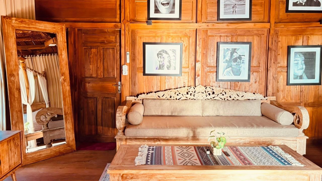 A cozy room with a wooden sofa, a mirror, and framed artwork on the walls.