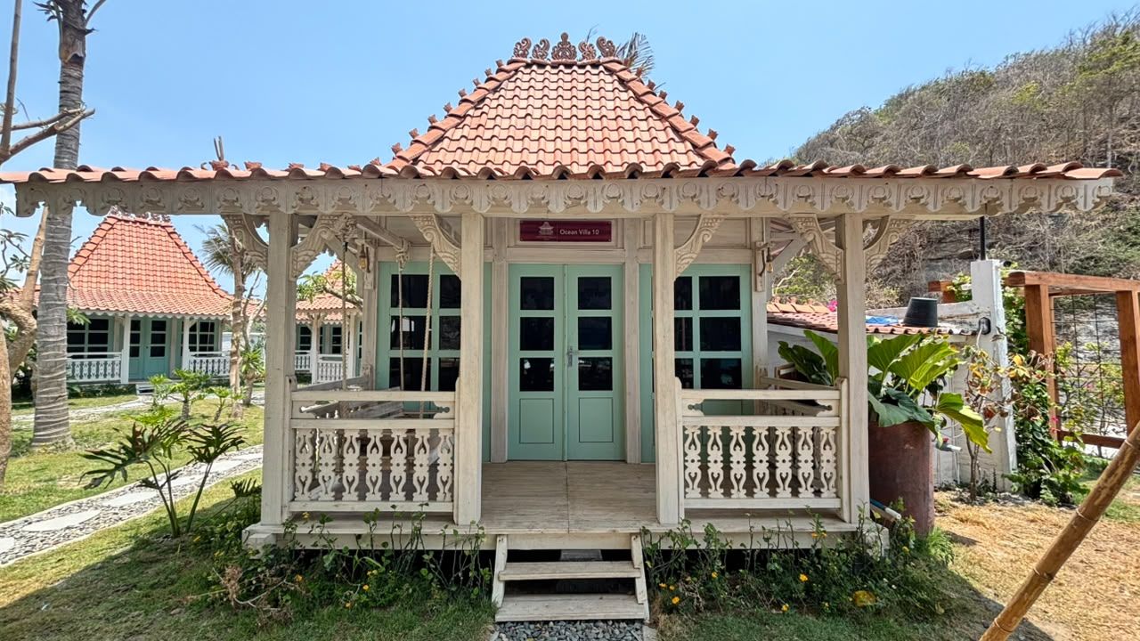 Um edifício em estilo tradicional com telhado de telhas, entrada central com porta verde e varanda com grades.