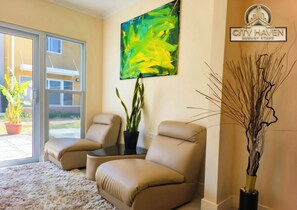 A room with two beige chairs, a large abstract painting, a potted plant, and a decorative vase. - City Haven | Luxurious 2BR Home • Modern & Secure (Portmore)