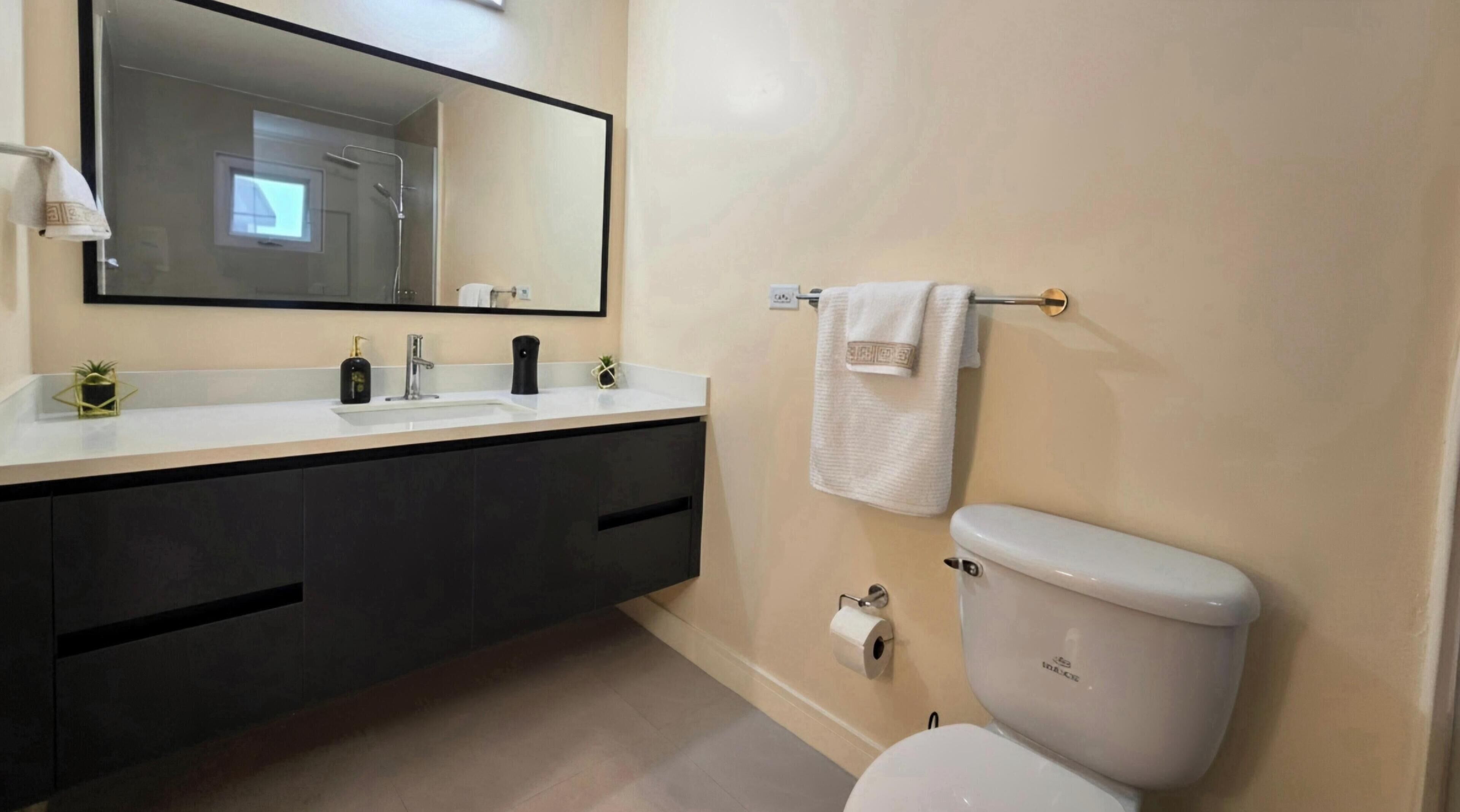 A modern bathroom with a dual sink vanity, a toilet, and a large mirror.