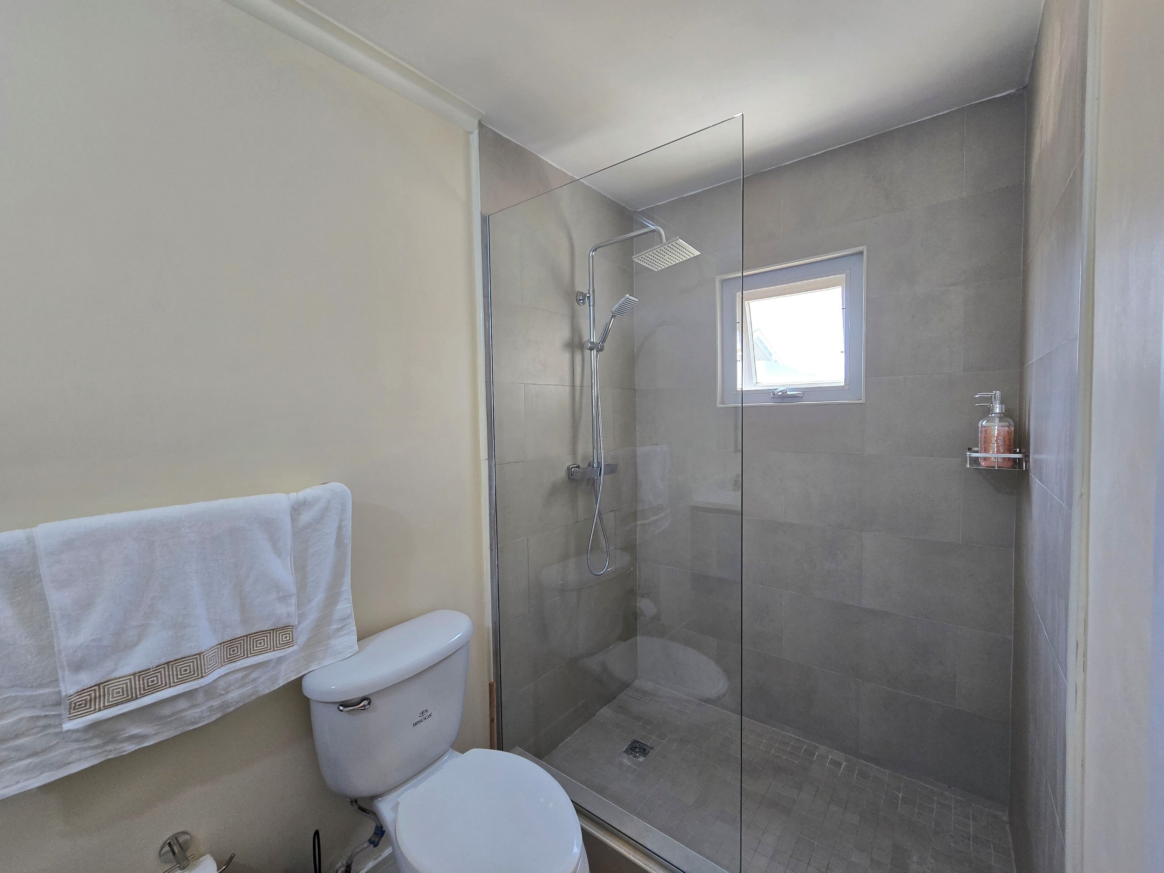 A bathroom with a toilet, a glass-enclosed shower, and a small window.