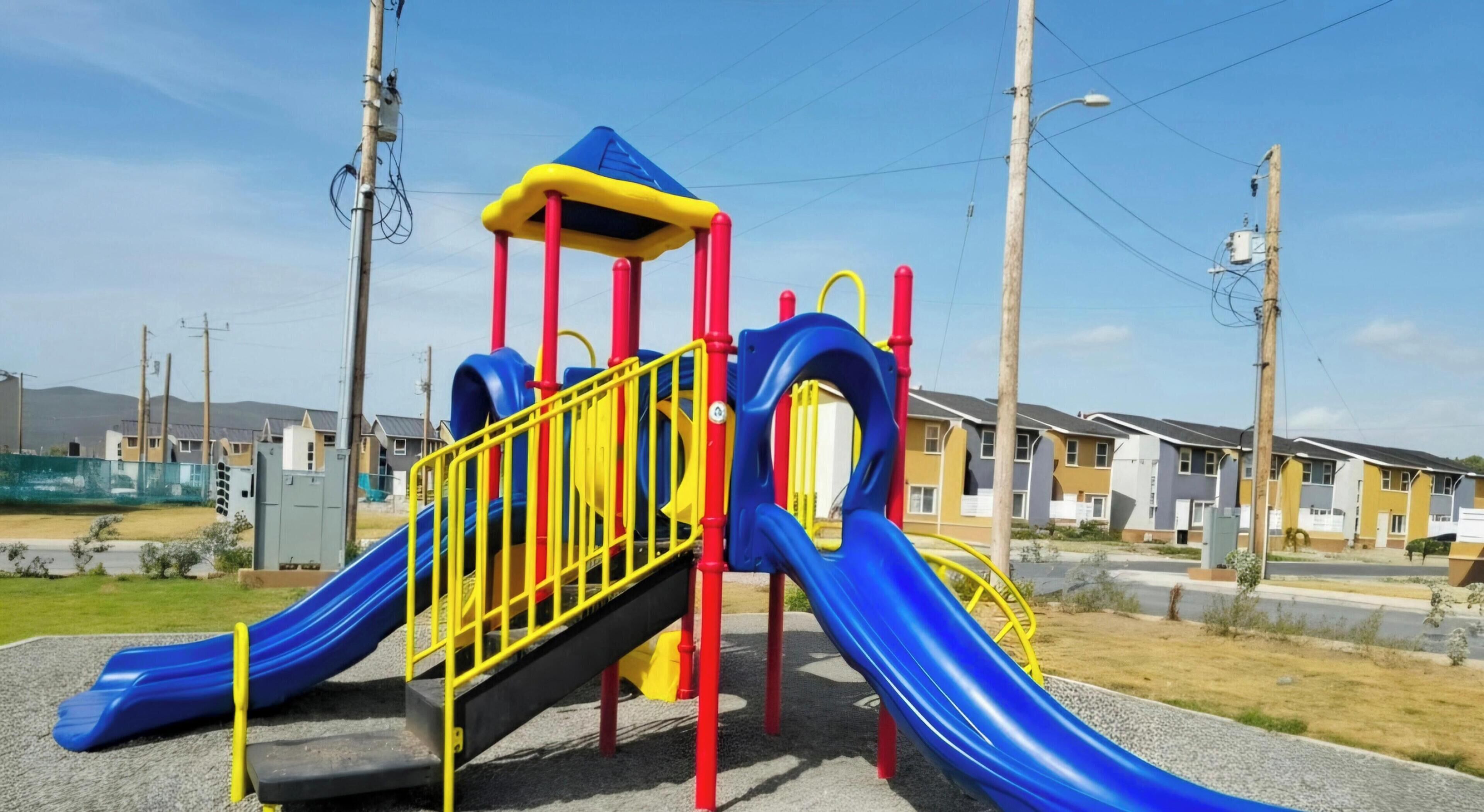A playground with a slide and climbing structures, surrounded by residential buildings.
