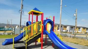 A playground with a slide and climbing structures, surrounded by residential buildings.