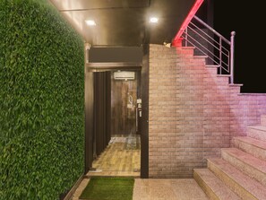 A building entrance with a wooden door, a staircase with red railings, and a green wall.