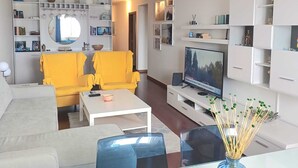A modern living room with a sofa, chairs, a coffee table, a TV, and a bookshelf.