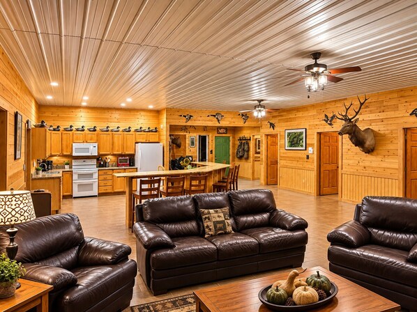 A spacious living area with leather sofas, a wooden dining table, and a kitchen with wooden walls and ceiling.