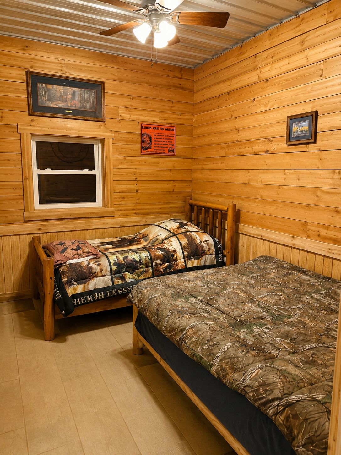 A cabin-style room with two wooden beds, a window, a ceiling fan, and a wildlife conservation sign.