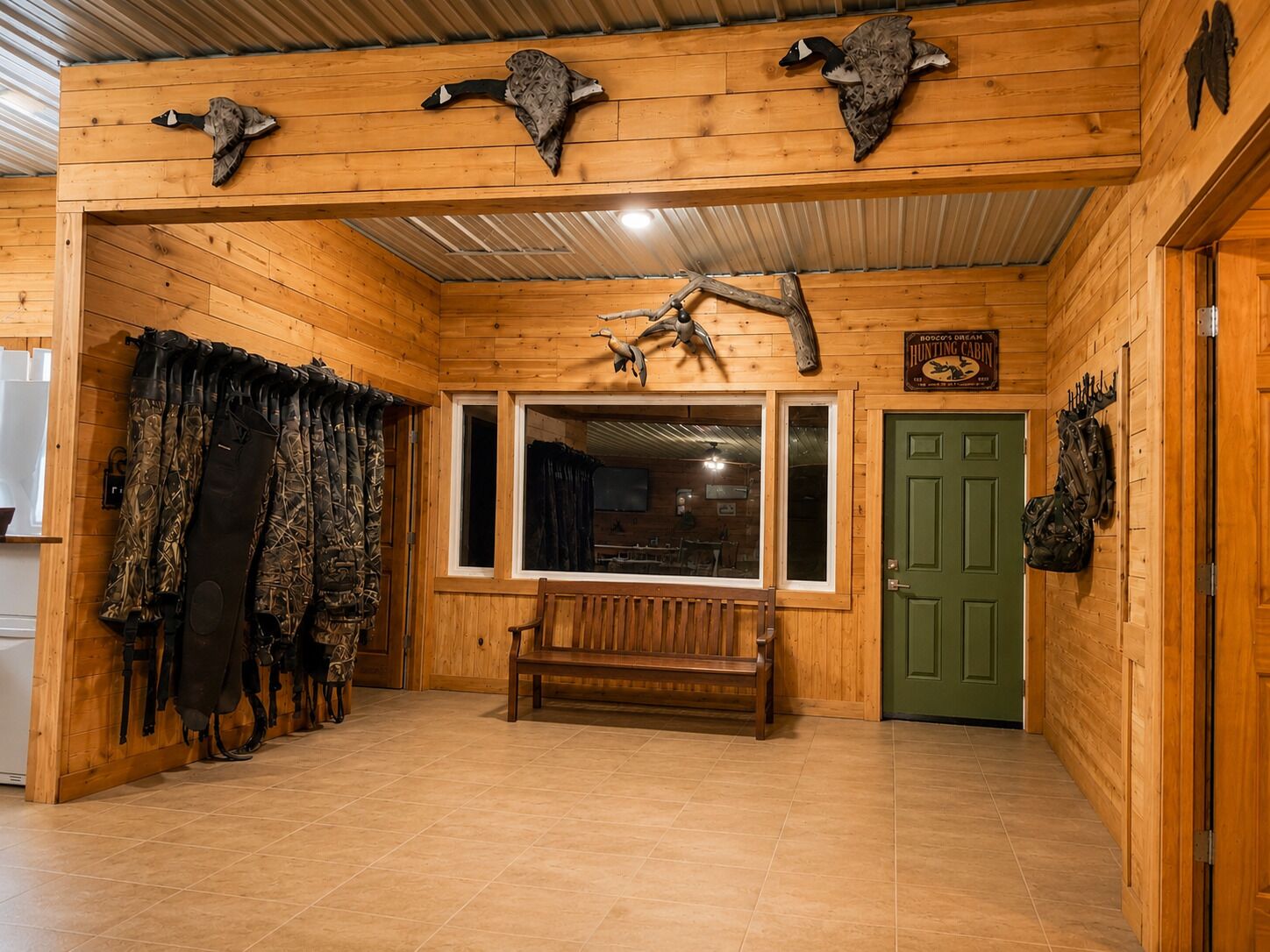 A cabin interior with wooden walls, a bench, hunting gear, and mounted animal heads.