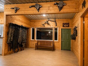 A cabin interior with wooden walls, a bench, hunting gear, and mounted animal heads.