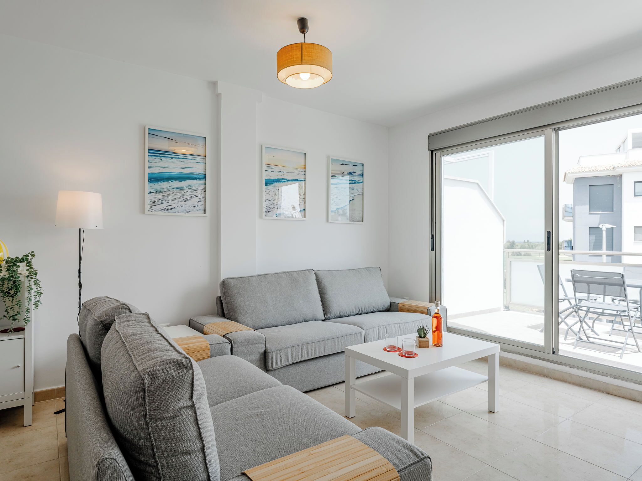 Una sala moderna con un sofá gris, una mesa de centro blanca y un ventanal con vistas al exterior.