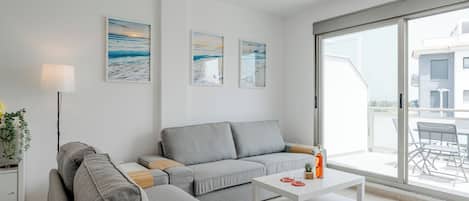 A modern living room with a grey sofa, a white coffee table, and a large window offering a view of the outside.