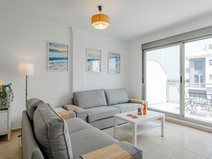 A modern living room with a grey sofa, a white coffee table, and a large window offering a view of the outside. - Oliva Nova Cabagua by Interhome (Oliva)