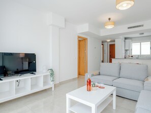 A modern living room with a flat-screen TV, a white coffee table, and a grey sofa. - Oliva Nova Cabagua by Interhome (Oliva)