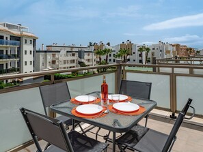 A balcony with a table set for four, overlooking a residential area with modern buildings and palm trees. - Oliva Nova Cabagua by Interhome (Oliva)