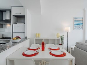 A modern kitchen with white cabinets, a built-in oven, and a dining area with a white table set for four. - Oliva Nova Cabagua by Interhome (Oliva)