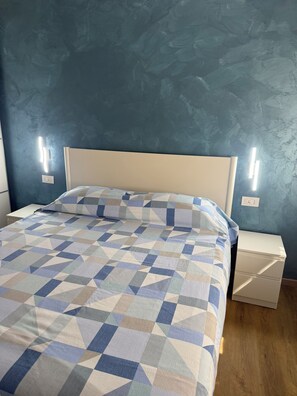 Ein Bett mit einem geometrisch gemusterten Überwurf, einem weißen Kopfteil und zwei Nachttischen mit an der Wand befestigten Lampen.